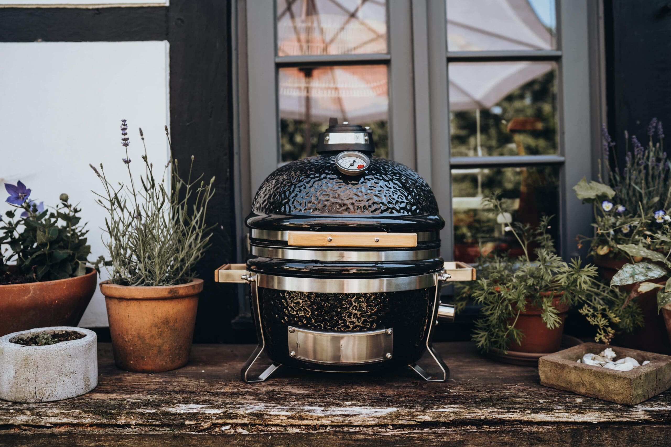 Monolith Icon kamado grill on a rustic wooden table surrounded by potted plants.