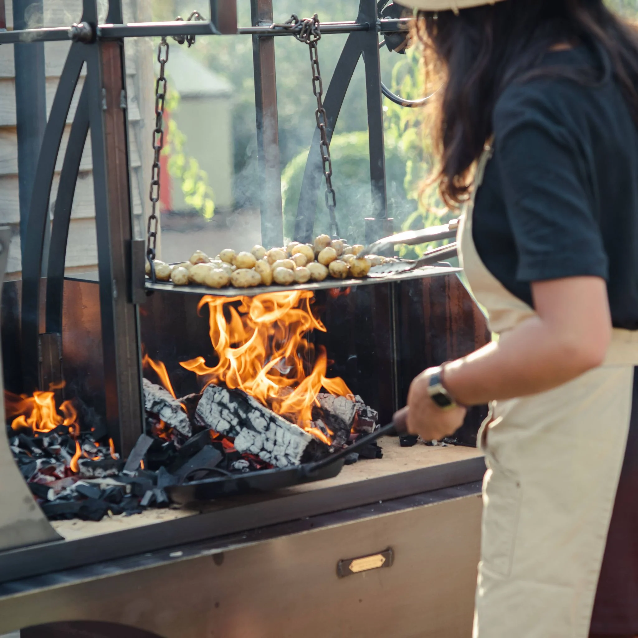 Person grilling potatoes over a wood fire on an Argentinian outdoor barbecue grill.