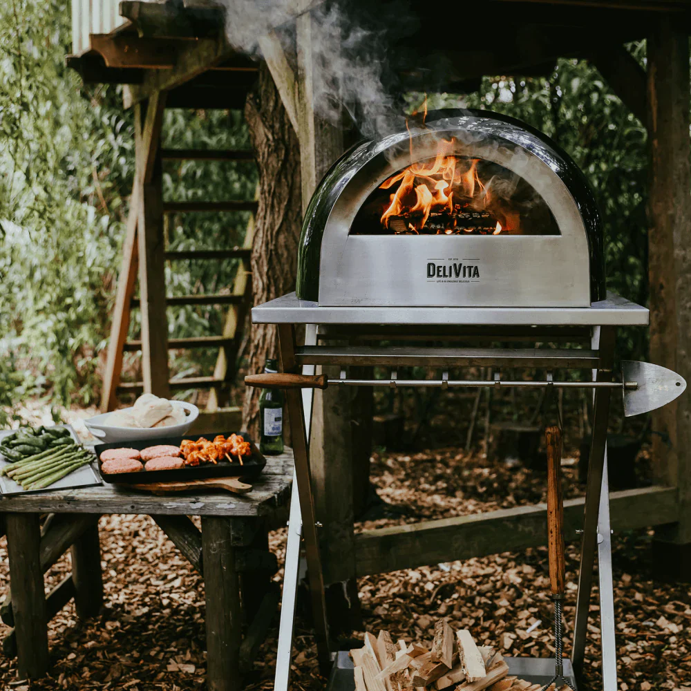 Delivita Emerald Green wood fired pizza oven on a stainless steel table with a fire burning inside.